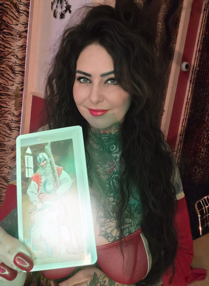 Tattoo: Bayo, ein Tattoo-Model, das eine erotische Tarotkarte in der Hand hält